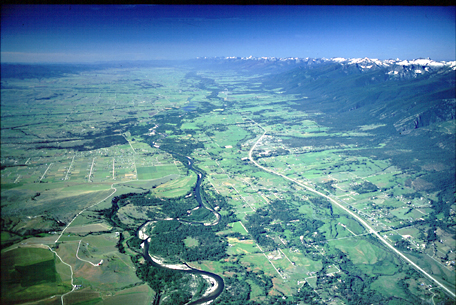 aerial photo of a broad valley with snow peak mountains on each side