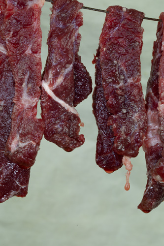 Juices drip from raw meat hanging on a string