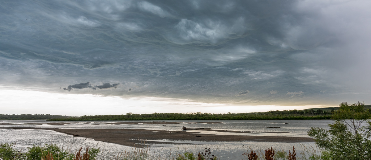 Storm clouds gathering over shallow river bank with flat forest expanse in the distance
