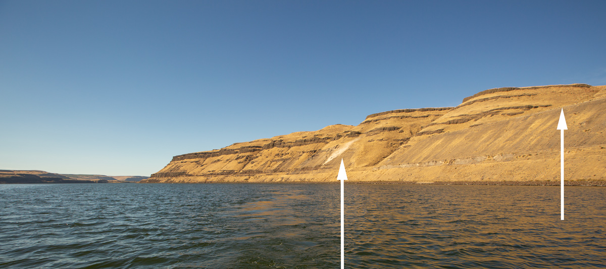 Dust cloud on a barren hill with layers of dark rock