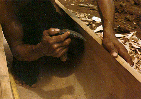 Native smoothing the inside of a dugout canoe with a rounded scraper