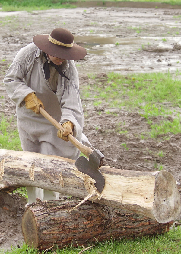 A broad axe is used to square a log on a rainy day