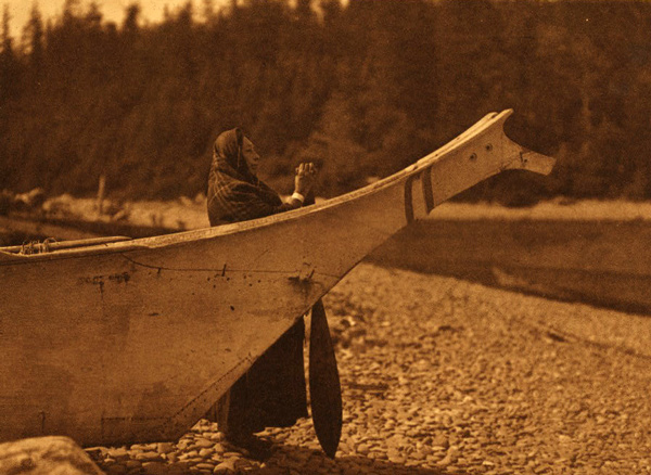 A Pacific Northwest coast Indian women stands next to her canoe gazing at the water