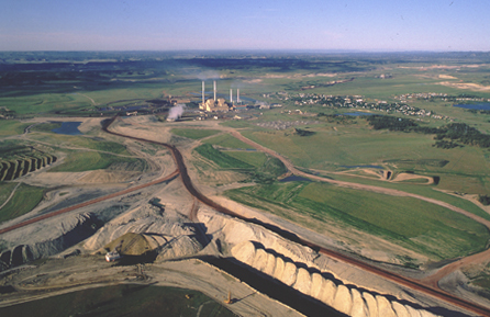 Large piles of dirt next to a railraod leading to a refinery with smokestacks